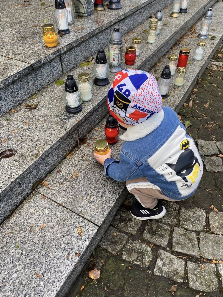 dziecko zapala znicz przy Pomniku Bojowników o Wolność i Niepodległość